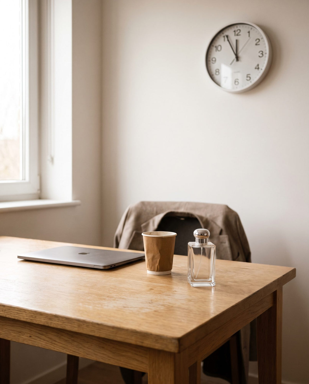 A perfume bottle on an office desk, the clock just before noon